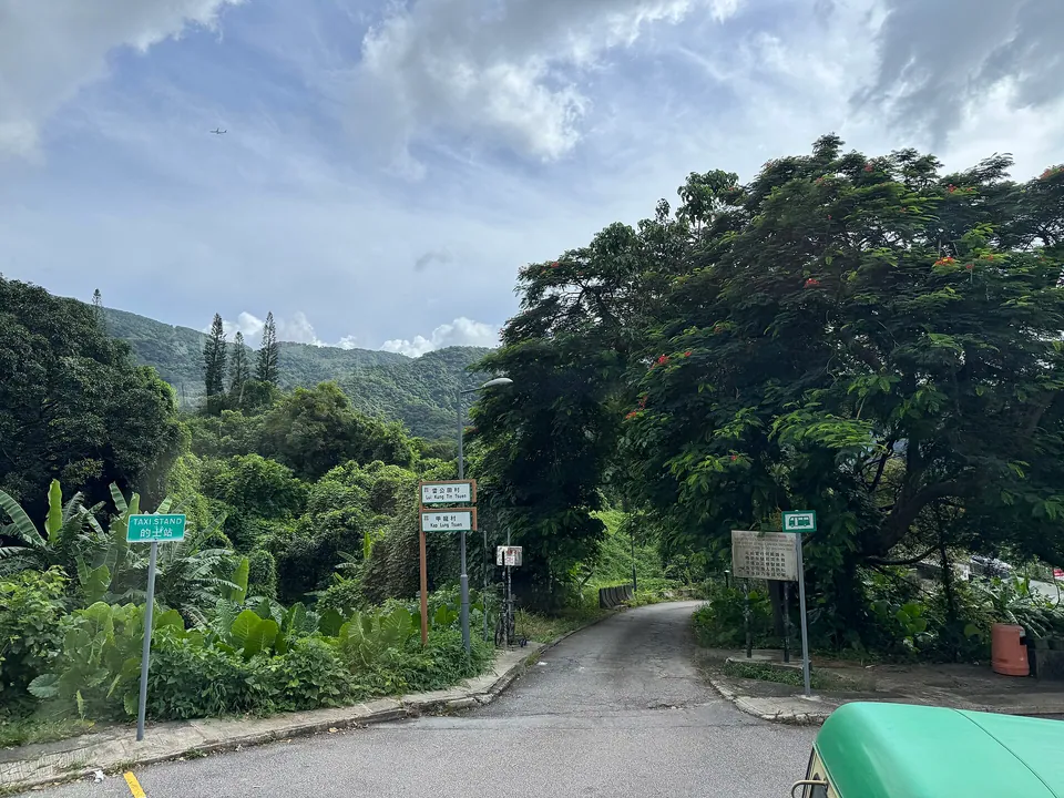 A lane leading off a road towards wooded hills, with signs for Lui Kung Tin Tsuen and Kap Lung Tsuen.