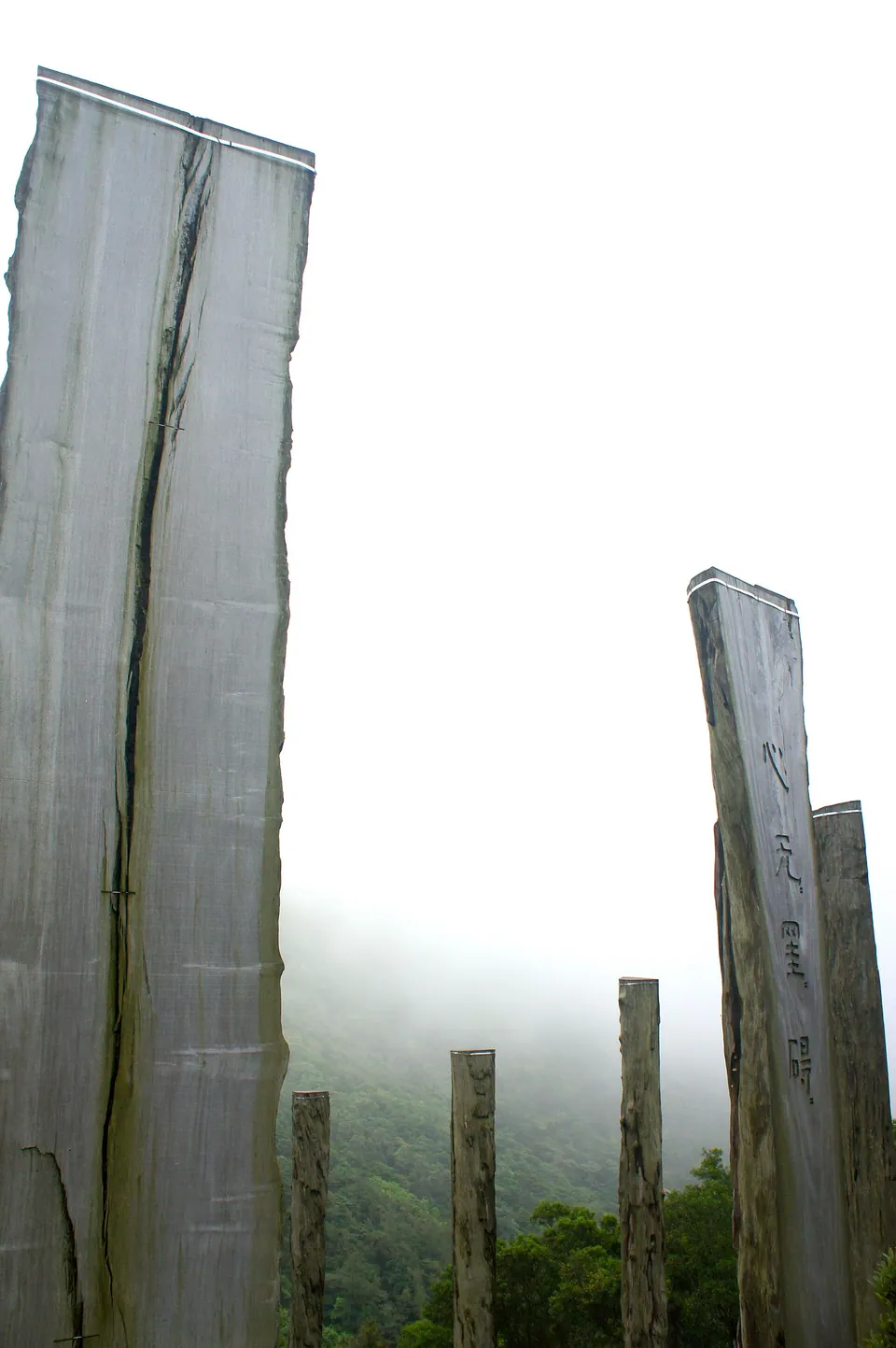 Tall wooden columns carved with Chinese text on a misty hillside.