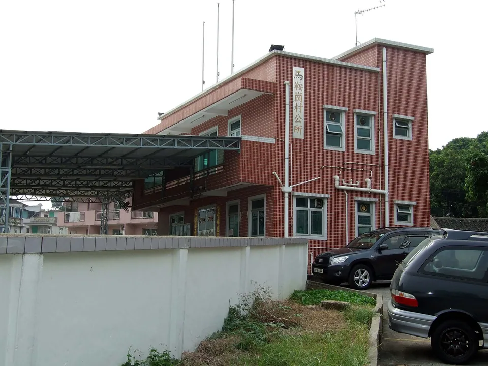 Two-storey red-tiled village office with the sign 馬鞍崗村公所, cars parked beside it.