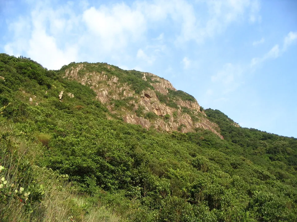 A steep green hillside with bare rock near the top under a blue sky.