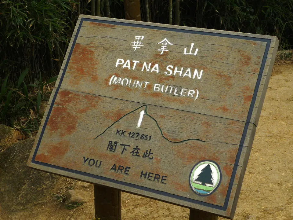 A weathered wooden board reading 畢拿山 Pat Na Shan (Mount Butler), You are here.