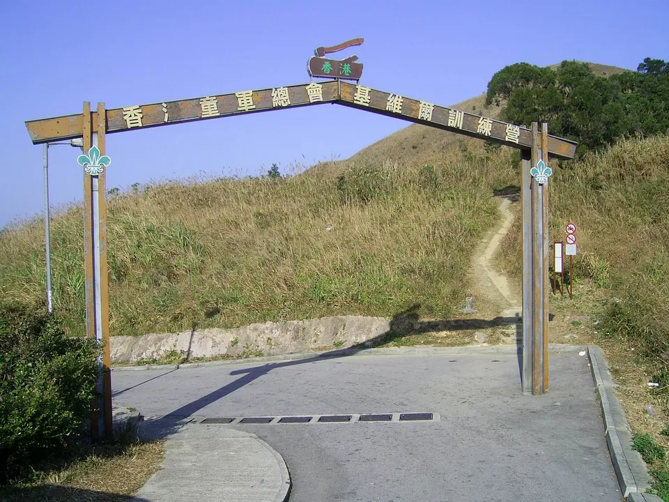 A wooden arch with Chinese lettering over a path leading up a grassy hillside.