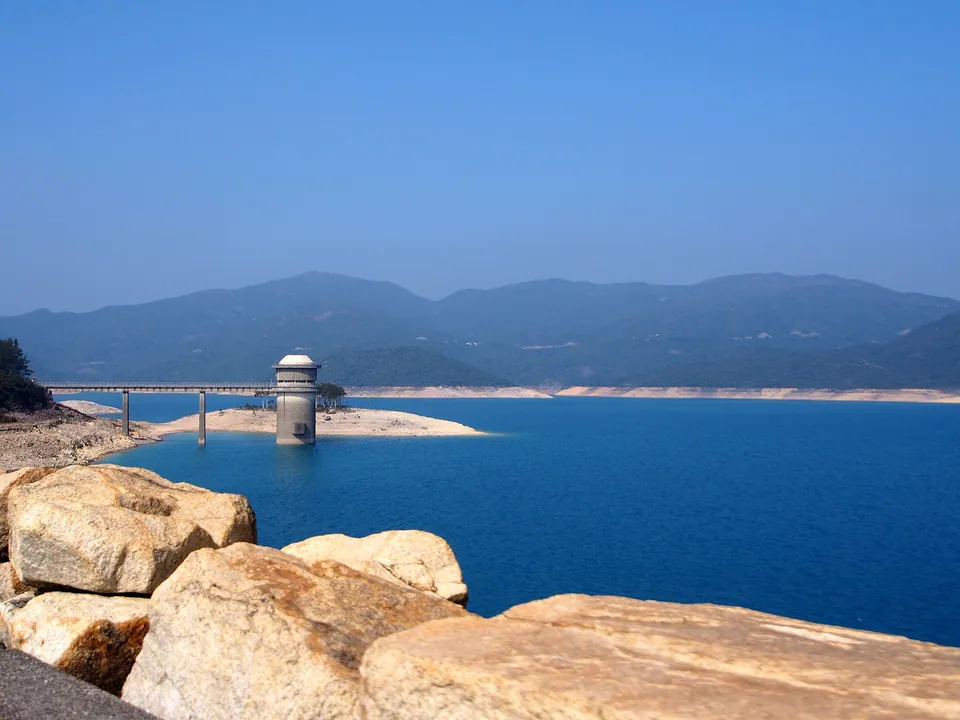 A deep blue reservoir with a cylindrical tower and a bridge, rocks in the foreground.