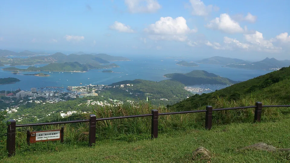View from a grassy plateau with a wooden fence over a town, a bay and many islands.